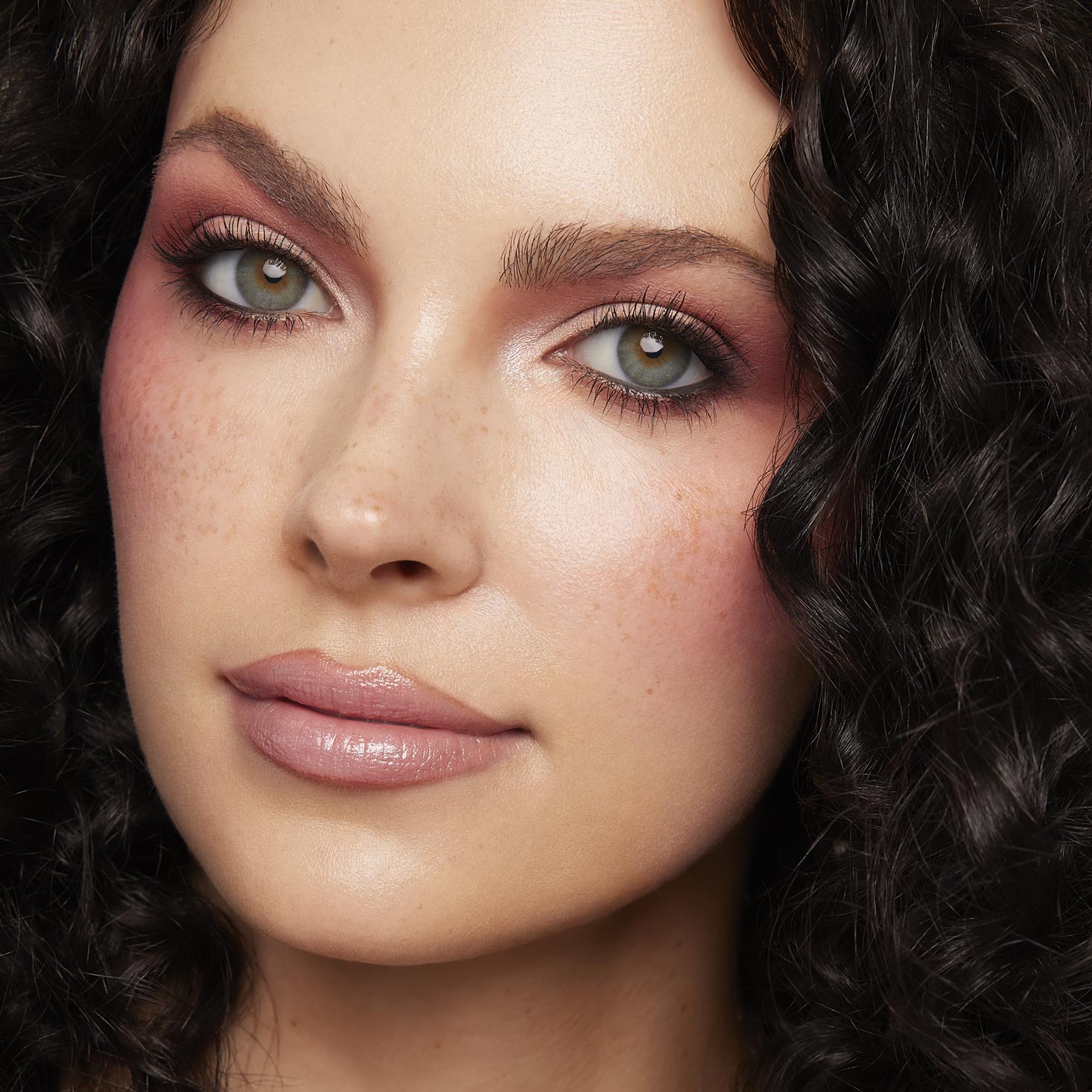 Rosy mauve eyeshadow with soft brown crease and inner-corner shimmer on a model, showcasing the Coconut BB ColourPop Shadow Palette Set, with long lashes, nude glossy lips, freckles, and dark curls in a studio close-up.